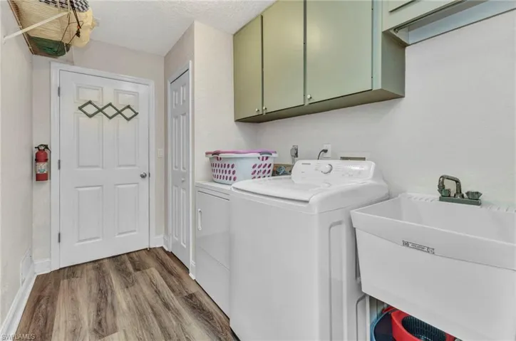 Laundry room featuring washing machine and clothes dryer, cabinet space, dark wood-style flooring, a sink, and a textured ceiling
