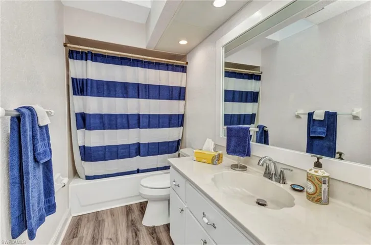 Bathroom with toilet, wood finished floors, a textured wall, vanity, and shower / bathtub combination with curtain