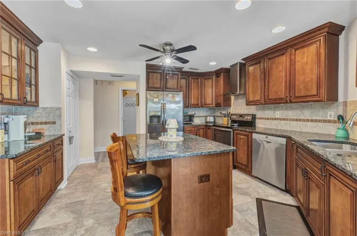 Kitchen with a kitchen bar, a sink, dark stone countertops, stainless steel appliances, and wall chimney exhaust hood