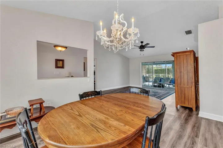 Dining room with wood finished floors, visible vents, baseboards, high vaulted ceiling, and ceiling fan with notable chandelier