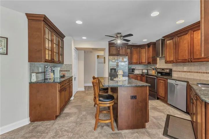 Kitchen featuring a kitchen bar, dark stone countertops, a kitchen island, appliances with stainless steel finishes, and wall chimney range hood