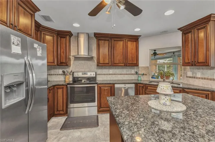 Kitchen featuring tasteful backsplash, visible vents, appliances with stainless steel finishes, wall chimney exhaust hood, and a sink