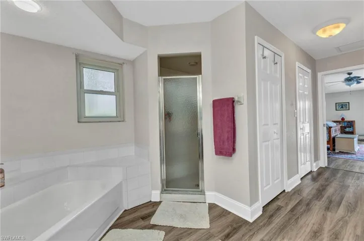 Bathroom featuring a stall shower, baseboards, a garden tub, and wood finished floors