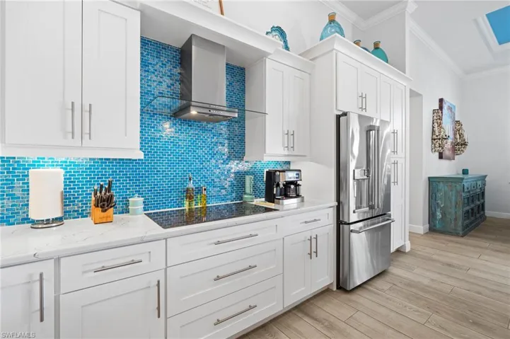 Kitchen featuring white cabinetry, high end refrigerator, ornamental molding, wall chimney range hood, and black electric cooktop
