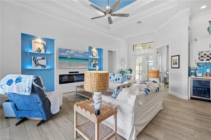 Living room with crown molding, wine cooler, bar area, french doors, and light wood-type flooring