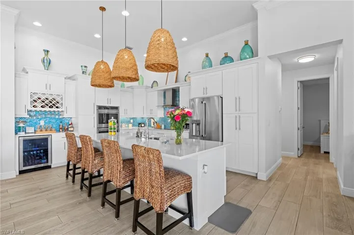 Kitchen featuring wine cooler, stainless steel appliances, an island with sink, and white cabinets