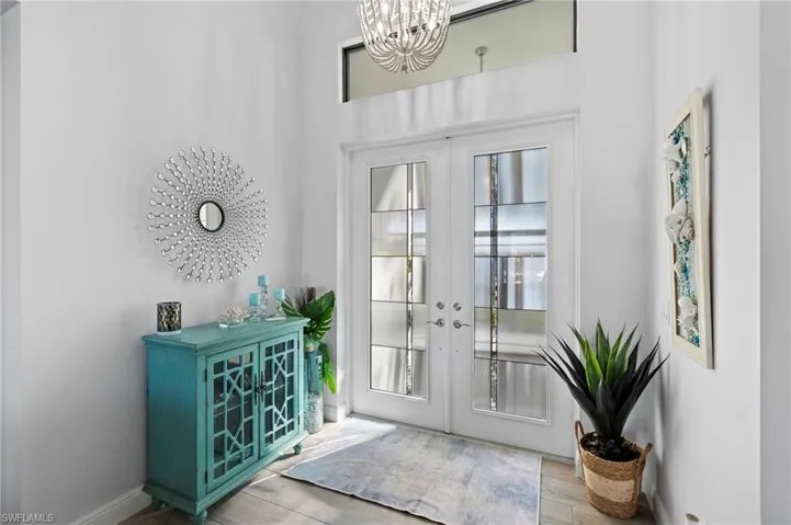 Entrance foyer with french doors, a healthy amount of sunlight, an inviting chandelier, and light hardwood / wood-style floors
