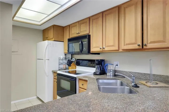 Kitchen with range with electric cooktop, black microwave, a sink, light tile patterned floors, and freestanding refrigerator