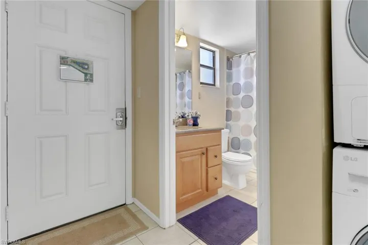 Full bathroom with stacked washer and clothes dryer, tile patterned flooring, vanity, toilet, and a shower with shower curtain