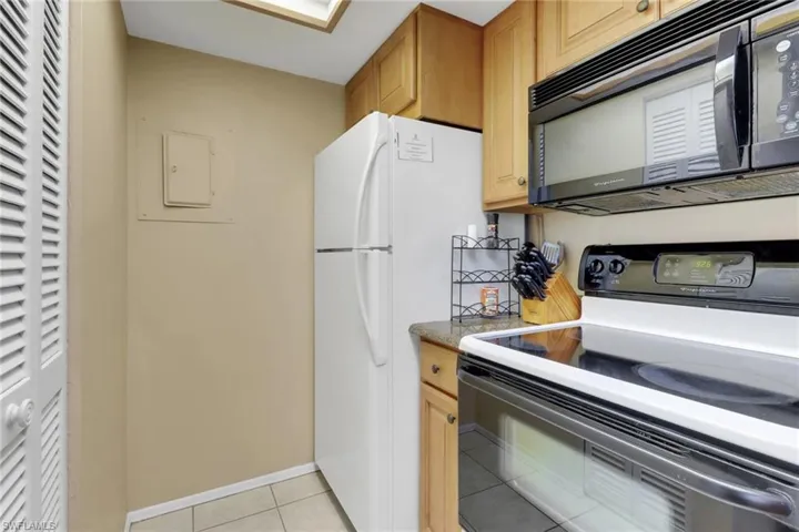 Kitchen with black microwave, range with electric stovetop, light tile patterned floors, freestanding refrigerator, and baseboards