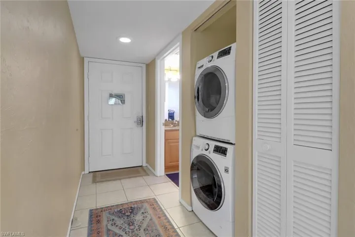 Laundry room featuring estacked washer and dryer, light tile patterned floors, baseboards, and recessed lighting