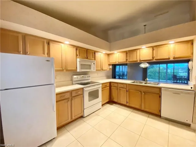 Kitchen featuring white appliances, light countertops, light tile patterned floors, and light wood finish cabinetry