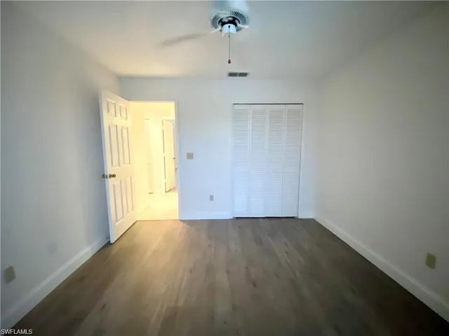 Unfurnished bedroom featuring dark wood-type flooring, a closet, and a ceiling fan