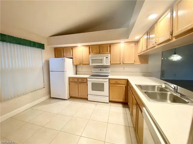 Kitchen featuring white appliances, lofted ceiling, light countertops, light tile patterned flooring, and light wood finish cabinets