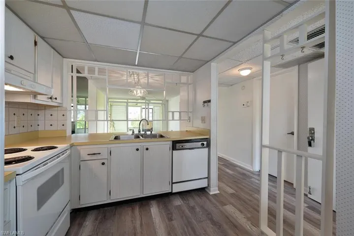 Kitchen with backsplash, white appliances, a paneled ceiling, white cabinets, and sink