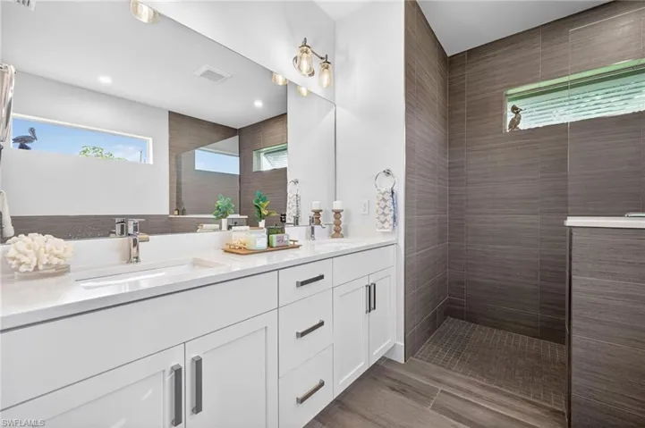 Full bath featuring double vanity, a walk in shower, and dark wood finished floors
