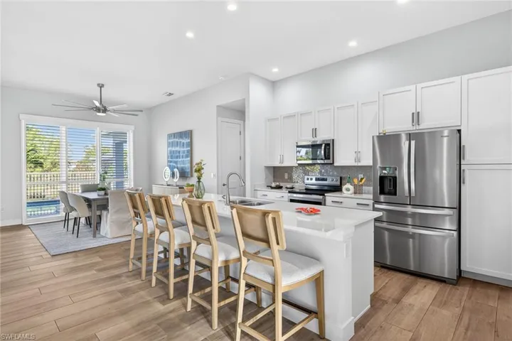 Kitchen with stainless steel appliances, white cabinets, a ceiling fan, an island with sink, and a breakfast bar area