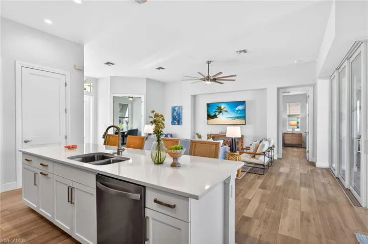 Kitchen featuring light wood-style flooring, stainless steel dishwasher, light stone counters, a center island with sink, and ceiling fan