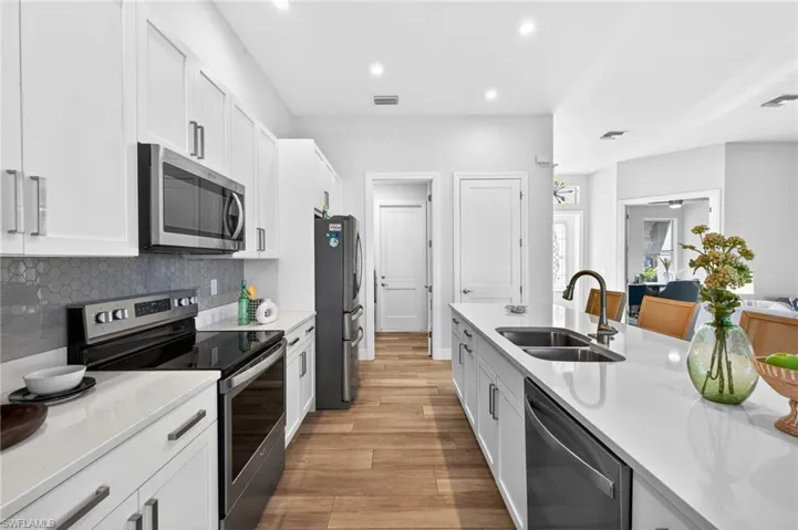 Kitchen with stainless steel appliances, white cabinets, light stone counters, light wood-type flooring, and recessed lighting