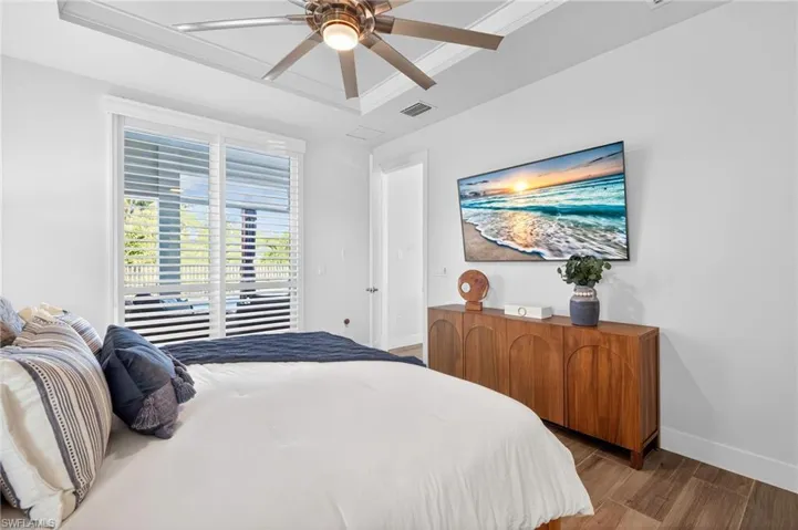 Bedroom with access to outside, wood finished floors, a tray ceiling, ceiling fan, and ornamental molding