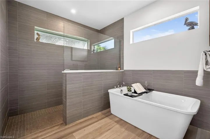 Full bathroom with tile walls, walk in shower, a freestanding bath, and light wood finished floors