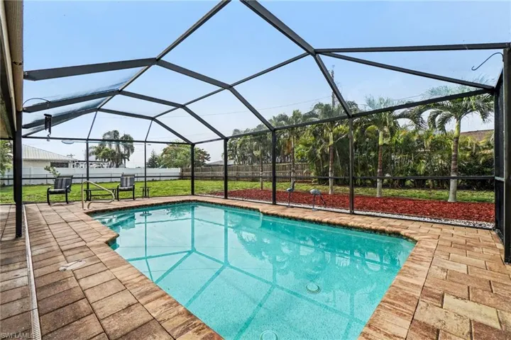 Screened pool enclosure with a rectangular swimming pool, paver deck, and surrounding landscaping