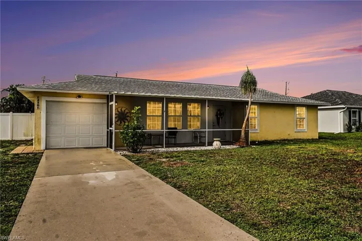 Screened front porch, attached garage, concrete driveway, mature palm tree, and a light-colored exterior finish