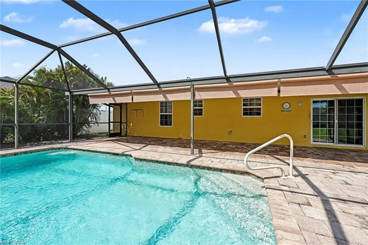 Screened-in pool deck featuring a clear blue swimming pool, paver hardscaping, a handrail for pool access, and sliding glass doors