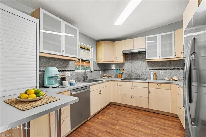 Wood-finish flooring, light wood cabinetry, stainless steel appliances, grey countertops, and a speckled backsplash