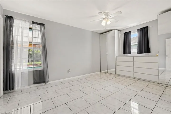 Expansive room featuring light tile flooring, a ceiling fan with light fixture, and two windows