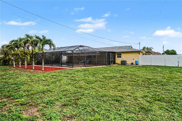 Expansive backyard featuring a screened pool enclosure, paved pool deck, and mature palm trees