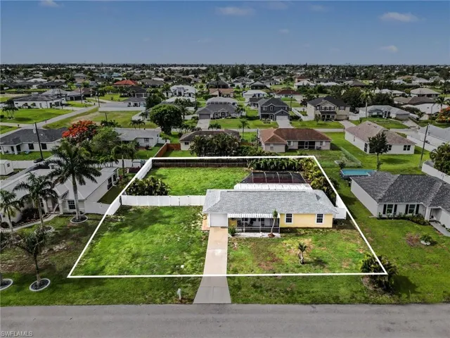 Expansive lot with a single-story residence, featuring a screened-in rear patio, mature palm trees, and a concrete driveway