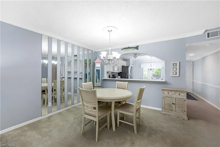 Dining space with light colored carpet, ornamental molding, a chandelier, and a textured ceiling