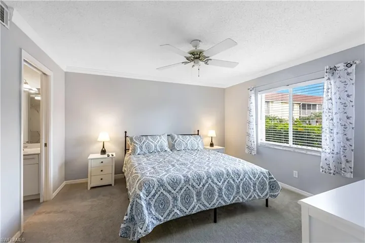 Carpeted bedroom featuring a textured ceiling, crown molding, a ceiling fan, and ensuite bath