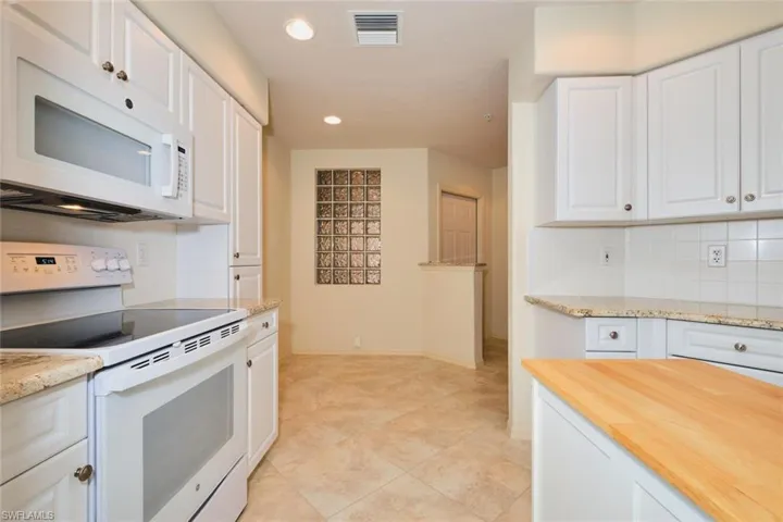 Kitchen with white appliances, decorative backsplash, recessed lighting, white cabinets, and light stone counters
