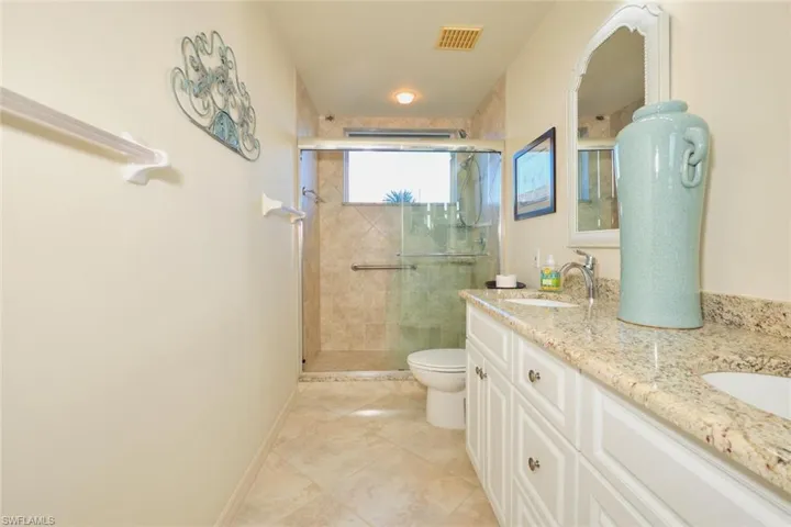 Full bath with double vanity, a shower stall, and light tile patterned floors