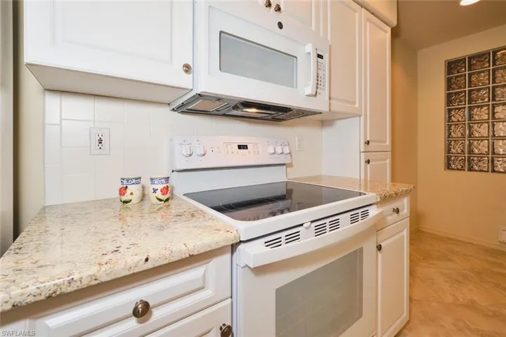 Kitchen with white appliances, light stone counters, white cabinets, backsplash, and light tile patterned flooring