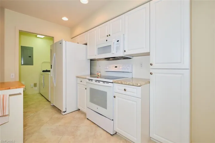 Kitchen with white appliances, white cabinetry, electric panel, light stone countertops, and light tile patterned flooring