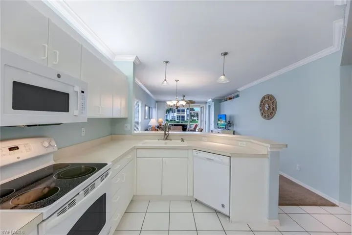 Kitchen featuring white appliances, hanging light fixtures, sink, white cabinets, and kitchen peninsula