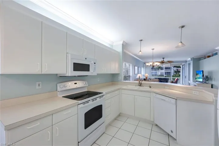 Kitchen with white cabinets, kitchen peninsula, crown molding, white appliances, and decorative light fixtures
