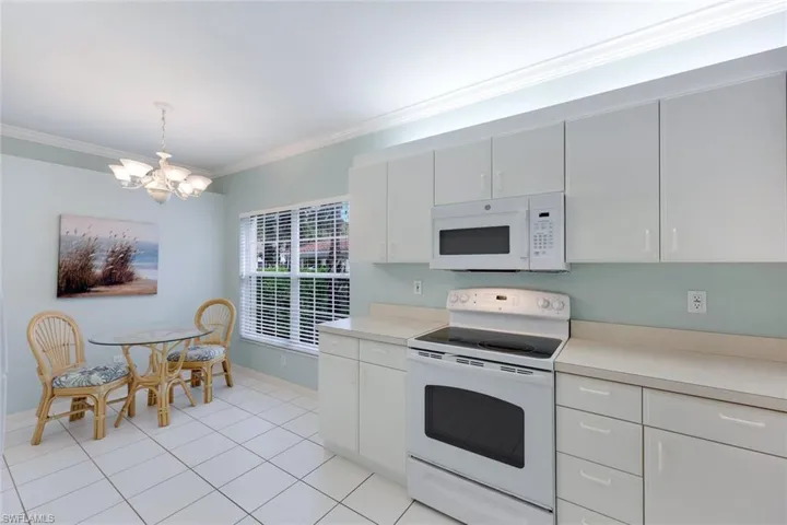 Kitchen featuring ornamental molding, white cabinetry, a notable chandelier, hanging light fixtures, and white appliances