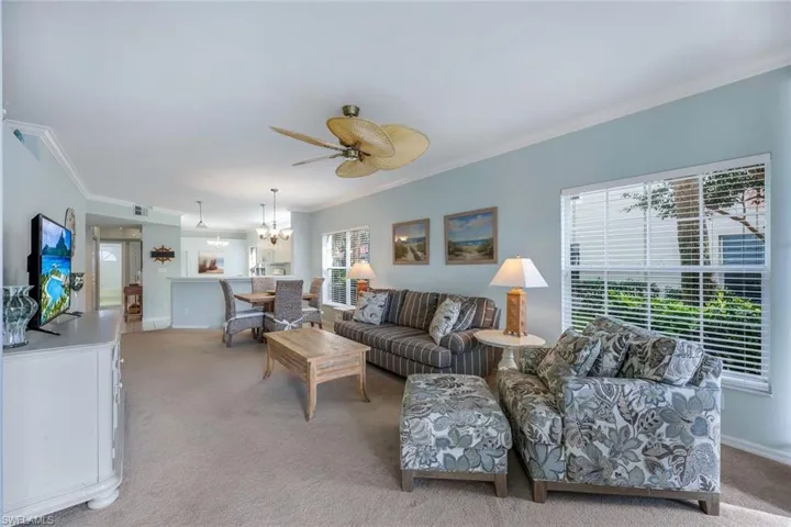 Carpeted living room featuring ornamental molding and ceiling fan with notable chandelier