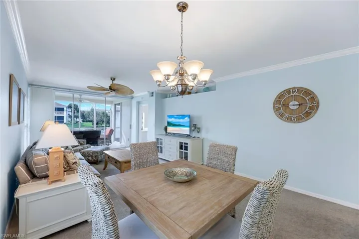 Carpeted dining room with ceiling fan with notable chandelier and crown molding