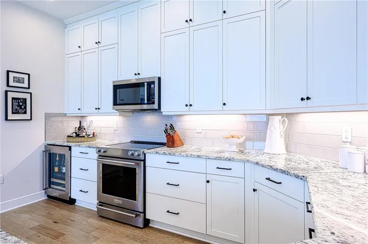 Kitchen featuring appliances with stainless steel finishes, light stone countertops, white cabinets, decorative backsplash, and beverage cooler