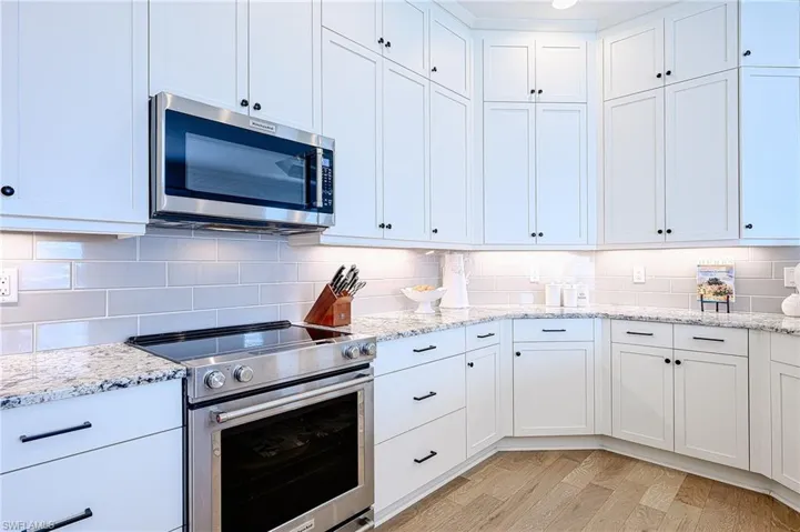 Kitchen with light stone counters, decorative backsplash, white cabinets, and appliances with stainless steel finishes