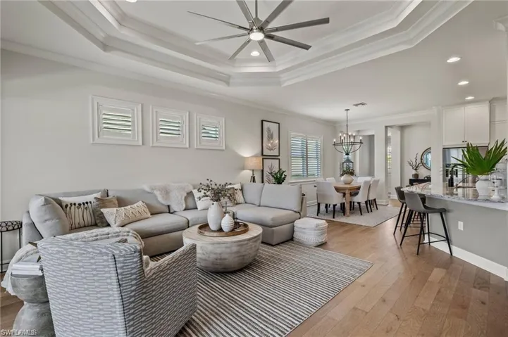 Living room featuring a tray ceiling, ornamental molding, light hardwood / wood-style floors, and ceiling fan with notable chandelier