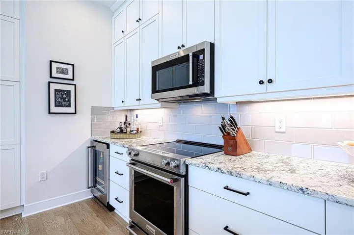 Kitchen with white cabinetry, appliances with stainless steel finishes, light stone counters, and decorative backsplash