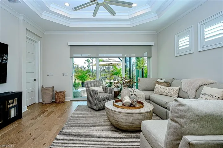 Living room featuring a raised ceiling, ornamental molding, ceiling fan, and light wood-type flooring
