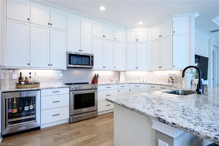 Kitchen featuring upgraded appliances with stainless steel finishes, white cabinetry, sink, beverage cooler, and light stone counters