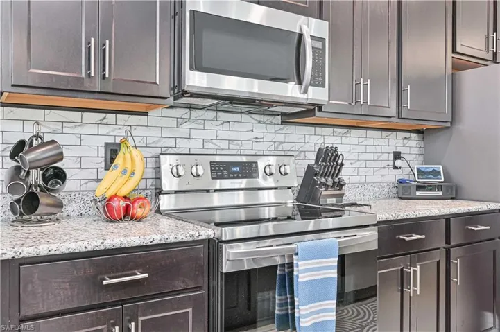 Kitchen featuring stainless steel appliances, light stone counters, tasteful backsplash, and dark brown cabinetry